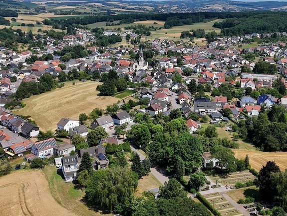 Blick über eine grüne Wiese Richtung Schwarzenholz. Ab Bildmitte sind die ersten Häuser zusehen. Schwarzenholz ist umrahmt von Natur.
